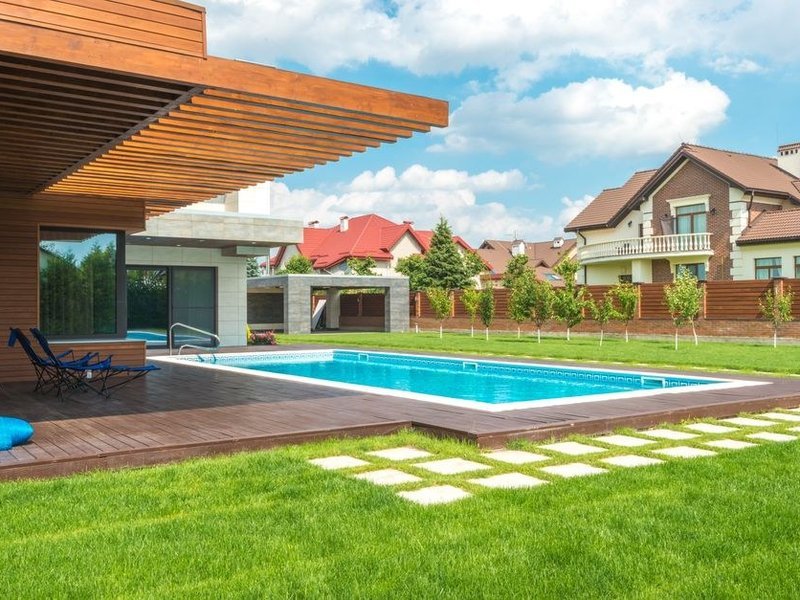 Terrasse de plain-pied autour d'une piscine dans une propriété d'Écully, grès cérame effet pierre posé sur plots dans la continuité du séjour