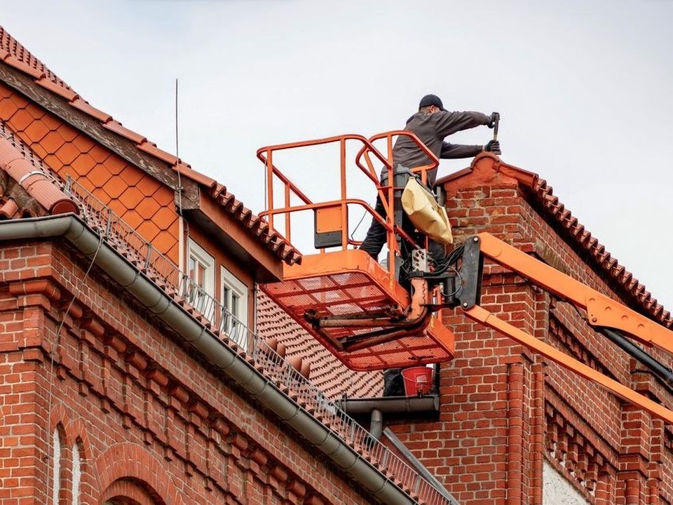 Couvreur intervenant sur la toiture en tuile à petite pente d'une maison de ville de Montchat à Lyon 3, gouttière pendante et lucarnes en façade