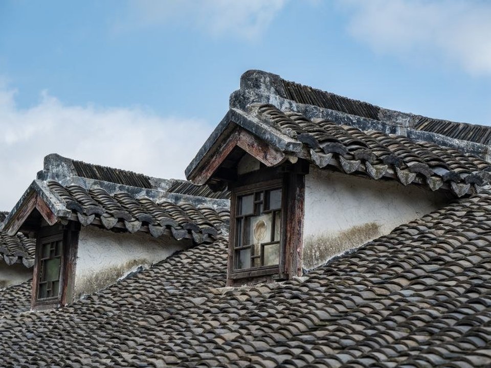 Couvreur intervenant sur la toiture très pentue en tuile canal d'un immeuble ancien du Vieux-Lyon, lucarnes en façade