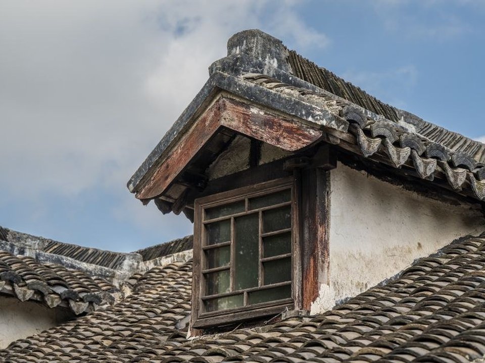 Couvreur reprenant la toiture en tuiles de terre cuite d'une maison ancienne du vieux bourg de Saint-Genis-Laval avec sa charpente traditionnelle en bois