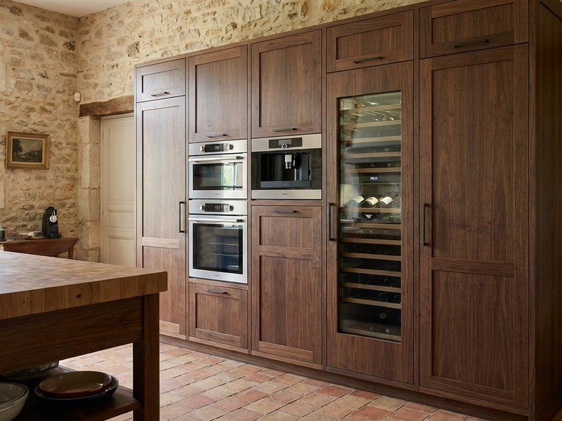 Mur de colonnes toute hauteur en bois massif intégrant fours encastrés, machine à café et cave à vin à façade assortie dans une cuisine haut de gamme d'Écully