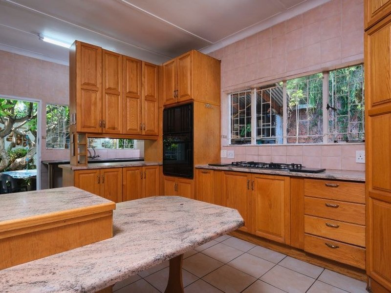 Cuisine ouverte d'une grande propriété boisée de Lentilly avec îlot central face au séjour, mur abattu et poutre posée, large baie donnant sur le jardin planté d'arbres