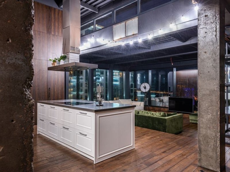 Cuisine îlot dans un loft de Confluence à Lyon 2 issu d'anciens docks, grande baie vitrée sur les bassins, verrière métallique et plan de travail contemporain, volume ouvert structuré par un îlot central