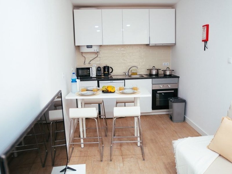 Cuisine équipée robuste et facile d'entretien posée dans un T2 locatif récent de Gerland à Lyon 7, façades pleines accordées au séjour, électroménager encastré et hotte discrète, ouverte sur le salon