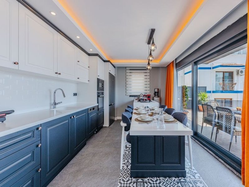 Cuisine d'une maison de Marcy-l'Étoile ouverte sur une terrasse par une large baie, plan de travail orienté vers les vallons boisés, lumière du plateau captée dans la pièce