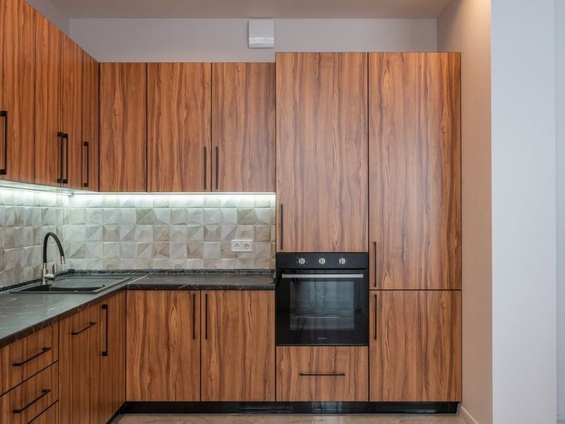 Cuisine compacte d'une maison de pierre du vieux bourg de Montrottier réagencée en L, rangements montant vers la hauteur sous plafond, lumière retrouvée et mur de pierre gardé apparent