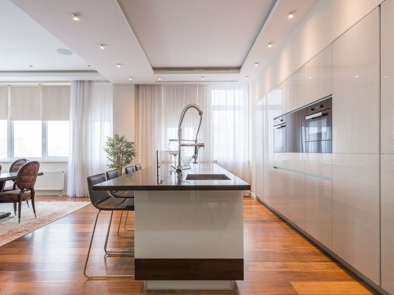 Cuisine à îlot ouverte sur le séjour dans un pavillon de lotissement de Saint-Genis-Laval, grand plan de travail familial et baie donnant sur la terrasse du jardin