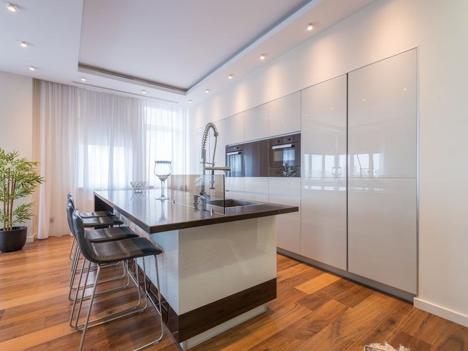 Cuisine à îlot central ouverte sur le séjour d'un pavillon individuel de Saint-Genis-Laval, grand plan de travail familial et baie donnant sur la terrasse et le jardin d'une maison de lotissement