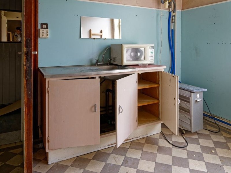 Cuisine fermée d'un appartement de copropriété des années 60-70 à Vénissieux avant réagencement, meuble bas ouvert sur les réseaux et la colonne technique existante