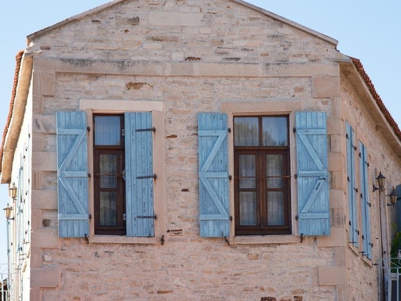 Volets battants bois repeints sur la façade en pierre d'une maison de carriers d'une ruelle pentue de Couzon