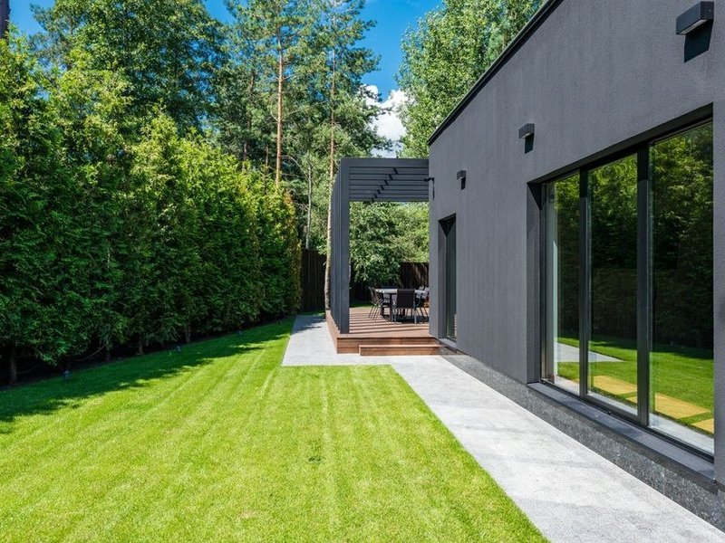 Grande baie coulissante sur-mesure en aluminium ouverte sur la pelouse et le parc plat d'une villa moderne d'Écully
