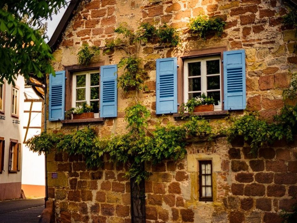 Maison de bourg en pierre de Pollionnay avec fenêtres et volets battants, au pied des coteaux boisés des Monts du Lyonnais