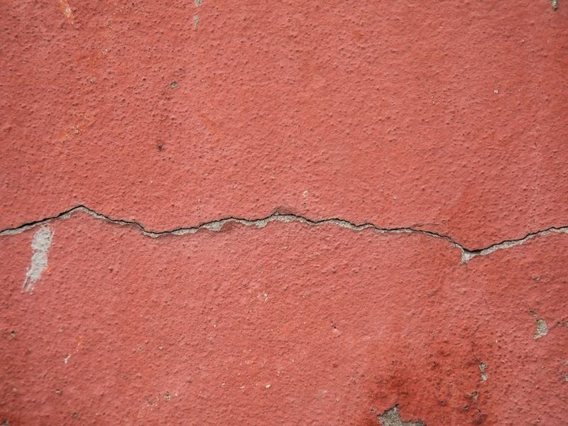 Faïençage et microfissures de dilatation sur l'enduit d'une façade de Bessenay chauffée au soleil, fentes garnies avant un revêtement souple