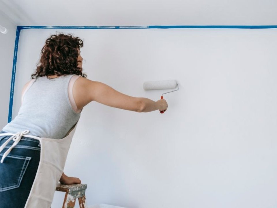 Peintre au rouleau posant une teinte claire sur le mur d'un séjour, pavillon résidentiel du bourg de Chassieu remis au propre