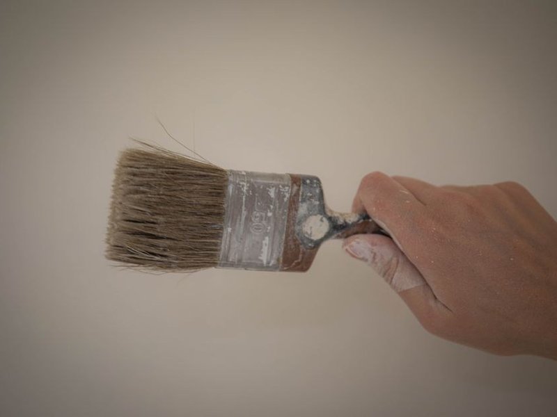 Peintre traçant une coupe nette à la bande entre le mur et le plafond d'un séjour de maison de coteau à Francheville, lumière verte filtrée par le jardin arboré