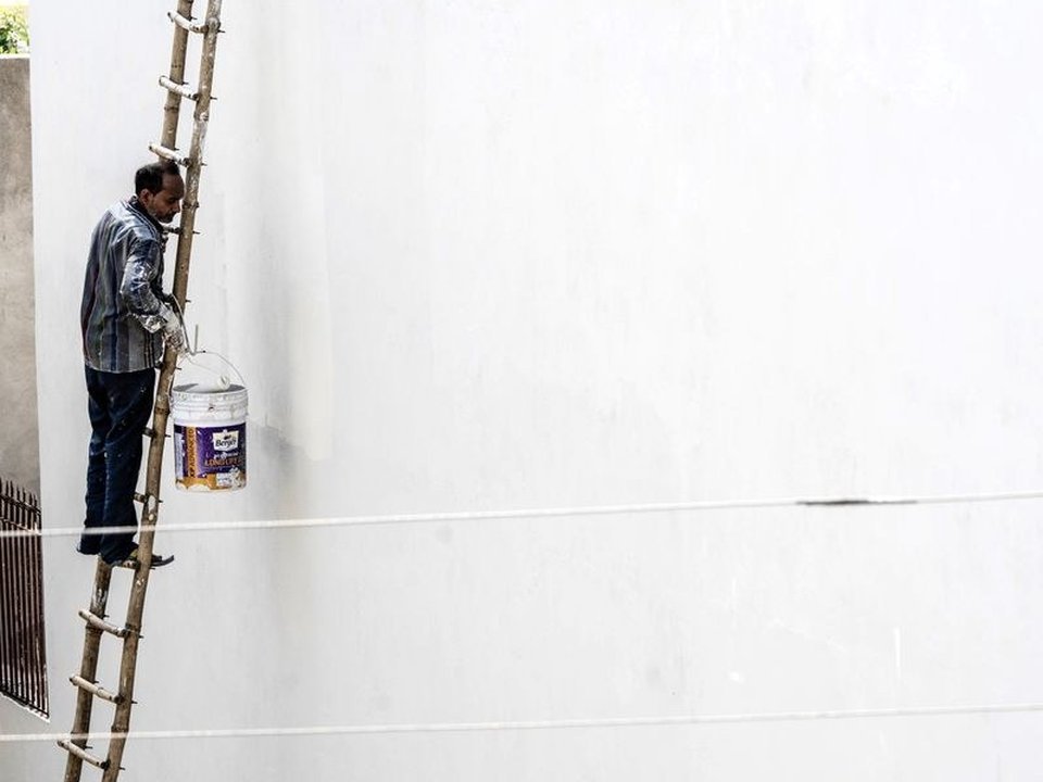 Artisan peintre sur plateforme peignant un grand mur en hauteur d'atelier dans un loft d'ancien atelier réhabilité de Vaise, Lyon 9, poutres métalliques et brique industrielle apparentes