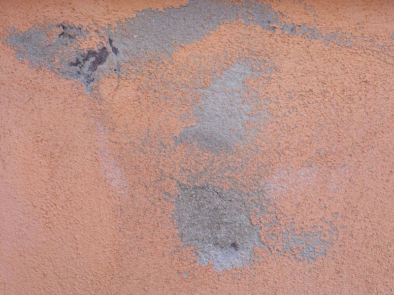 Traces blanches de salpêtre grattées et traitées sur le bas d'un mur en pierre d'une maison de ville ancienne d'Oullins avant remise en peinture
