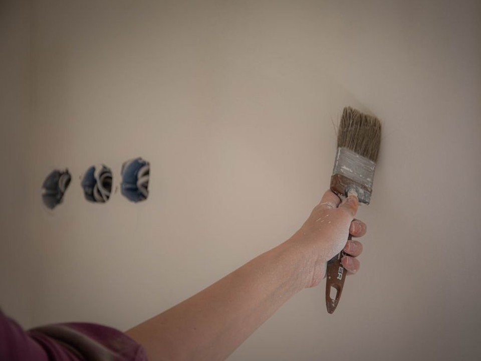 Artisan peintre appliquant au pinceau une sous-couche adaptée sur le bas d'un mur ancien en pierre et plâtre d'une maison de ville du vieux bourg d'Oullins, préparation du support avant peinture