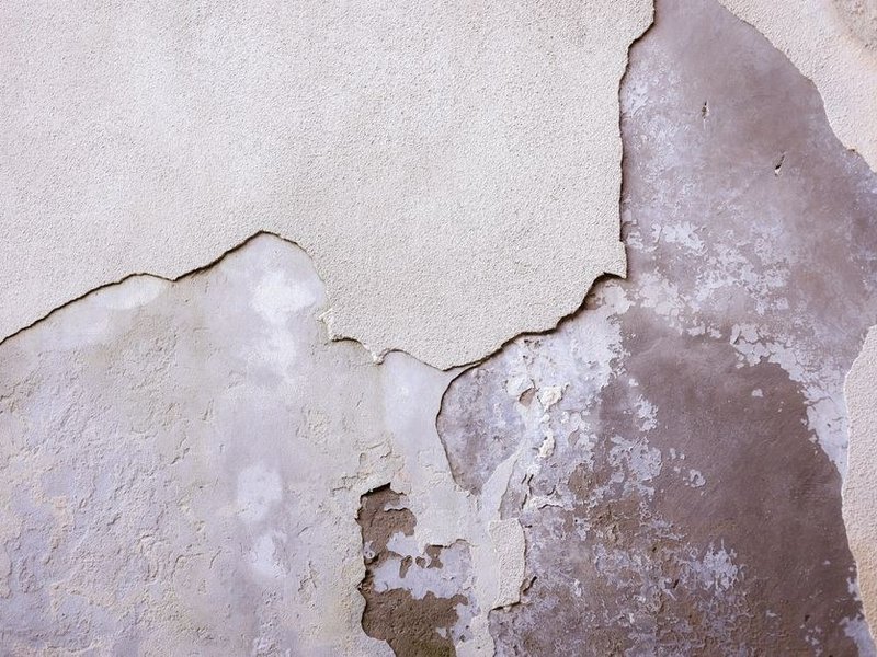 Mur de plâtre ancien écaillé dans une pièce basse d'une maison mitoyenne du bourg de Simandres, à reboucher et poncer avant peinture